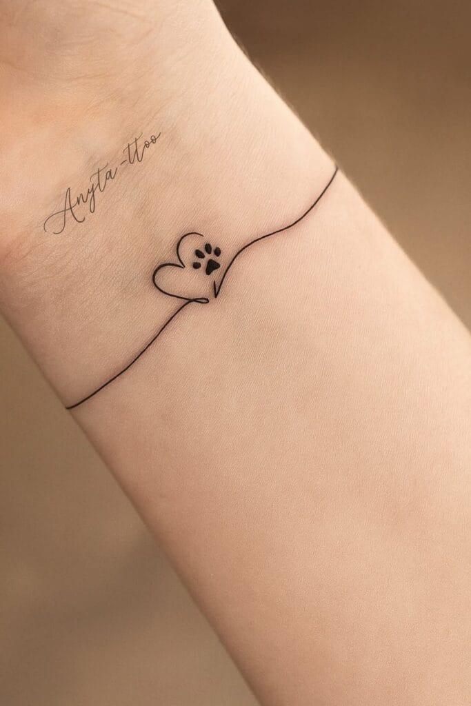 Close-up photograph of an actual wrist tattoo featuring a simple heartbeat line with a paw print, healed black ink, natural skin tone, person's hand relaxed on a neutral surface, natural daylight, fine line tattoo work, realistic texture and detail, professional tattoo photography, shallow depth of field, genuine tattoo not illustration