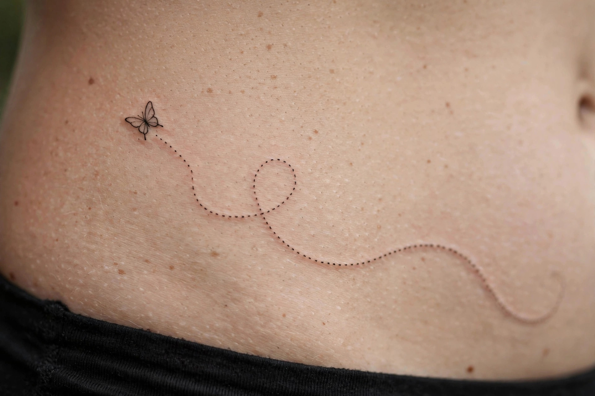 Small butterfly tattoo with dotted flight trail across waistline