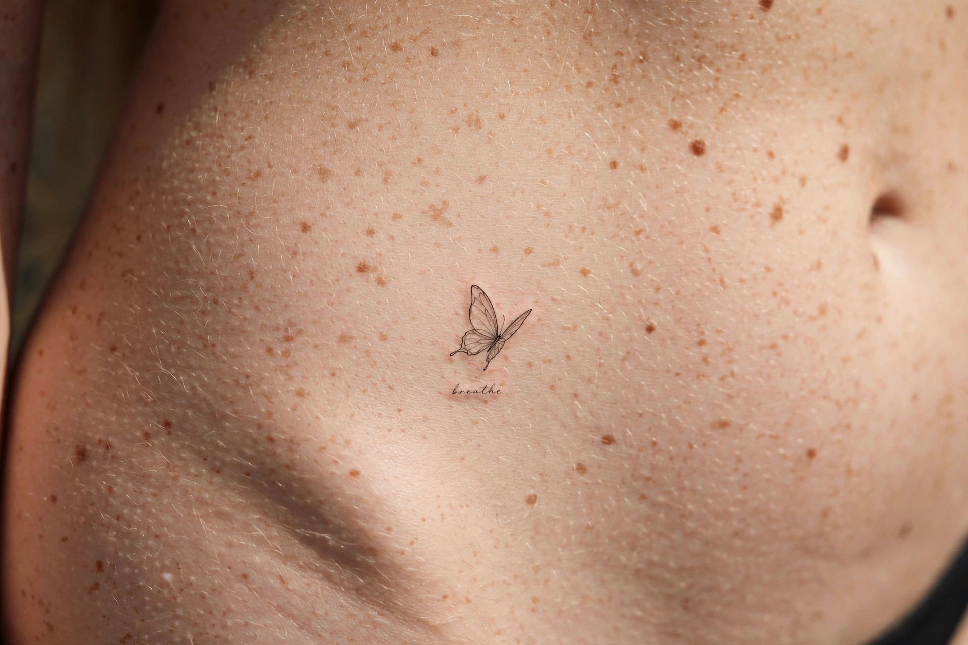 Fine-line butterfly waist tattoo with micro-script word