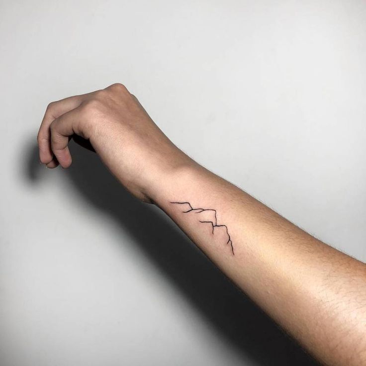 Minimalist mountain wrist tattoo with fine lines and geometric peaks on real skin