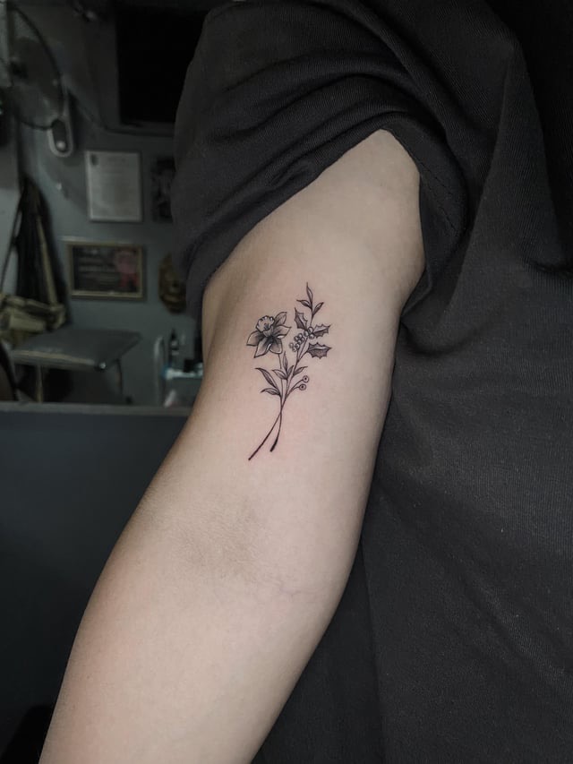 Delicate Floral Line Art Tattoo Delicate black ink tattoo of two crossed flowering plants on inner upper arm