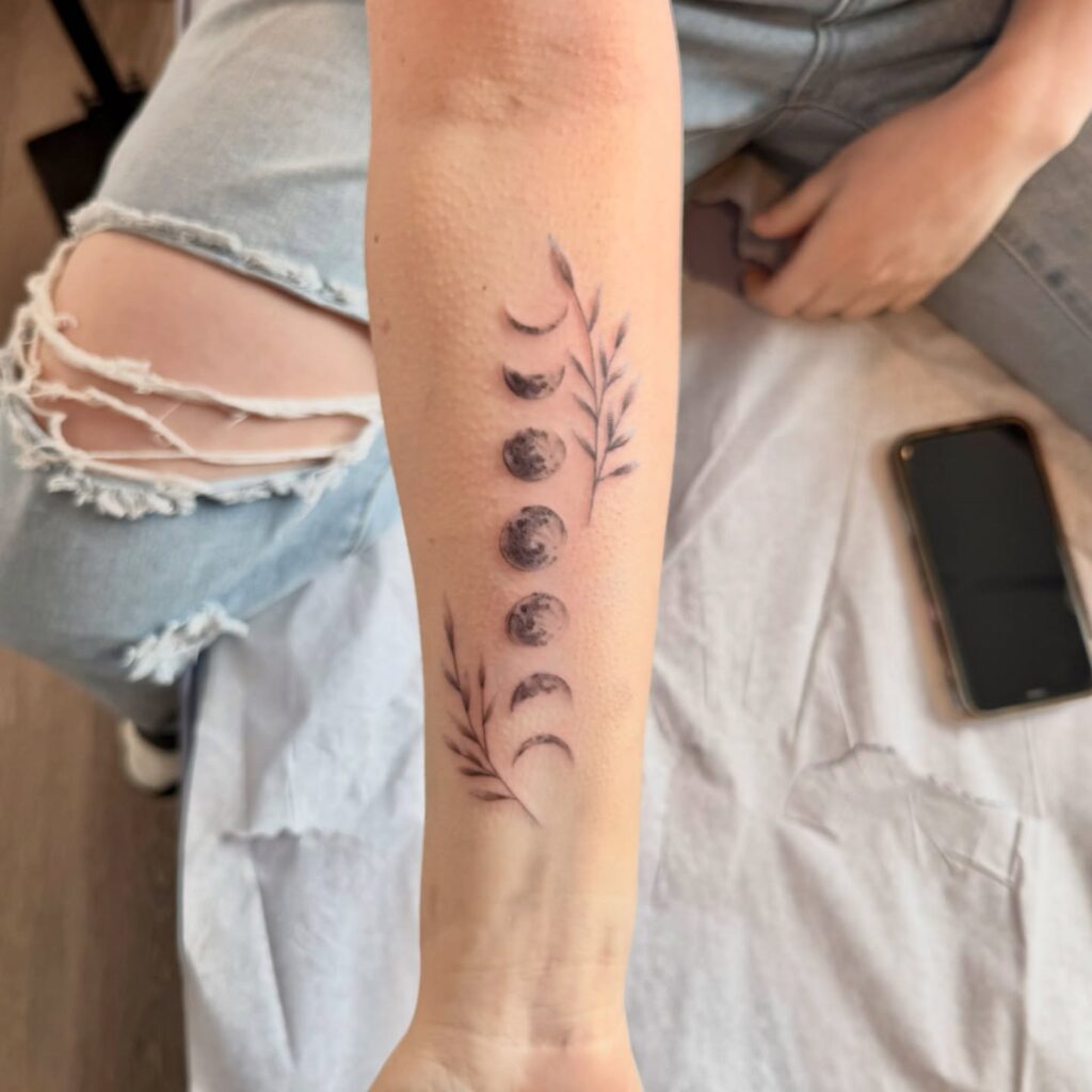 Botanical moon phases forearm tattoo