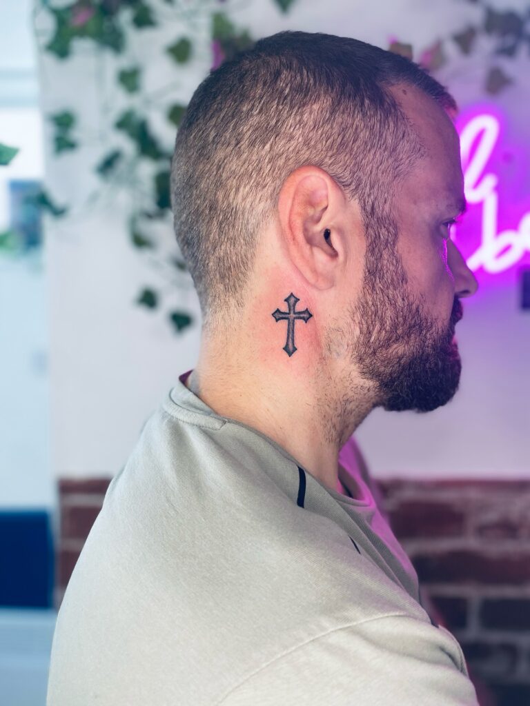 Classic black cross behind the ear tattoo
