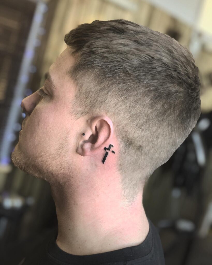 Simple clean cross behind the ear tattoo