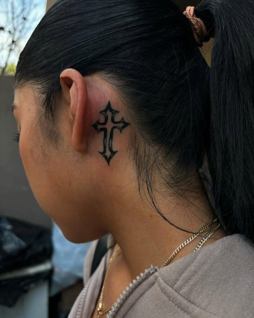 Dark gothic cross behind the ear tattoo