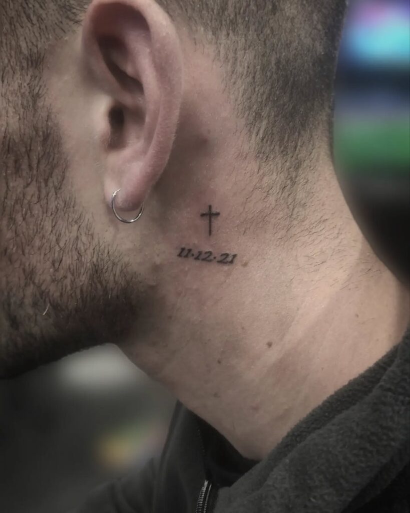 Cross with date behind the ear tattoo