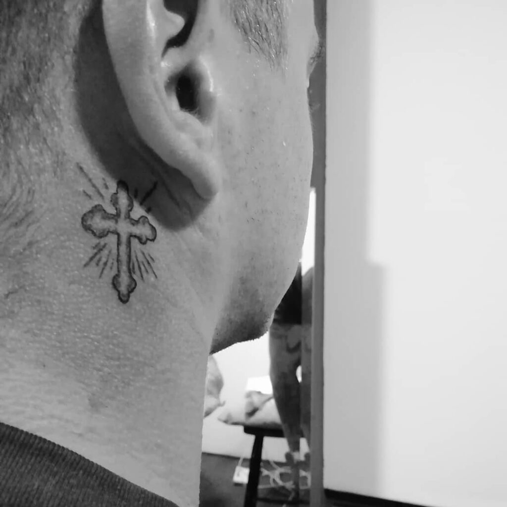 Radiant cross behind the ear tattoo with sunburst lines