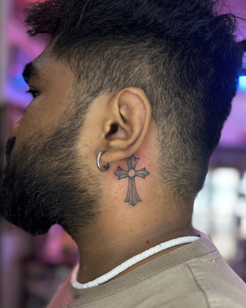 Shaded ornamental cross behind the ear tattoo