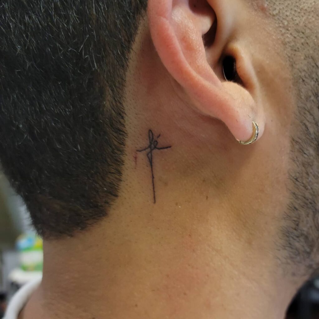 Cross with Fe script behind the ear tattoo