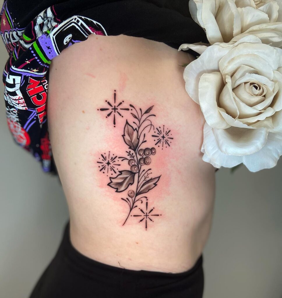 Sparkling Holly Sprig Tattoo on Ribcage december birth flower tattoo ideas tattoo