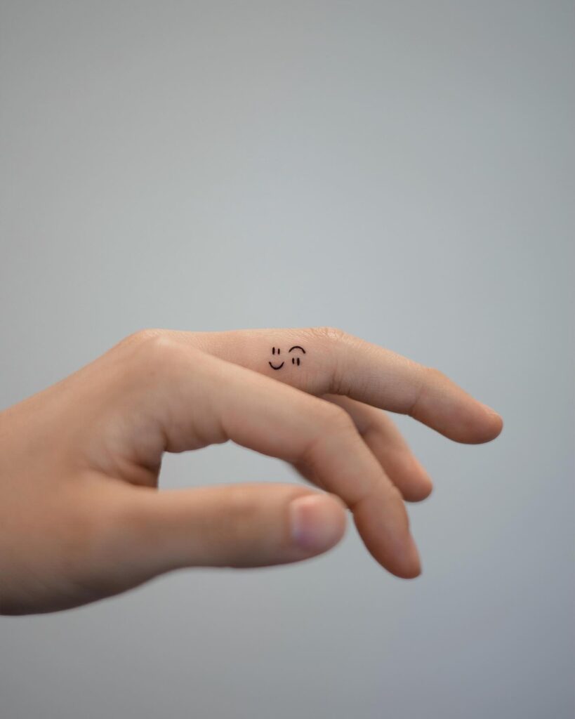 Tiny Winking Face Finger Tattoo meaningful tiny tattoos tattoo