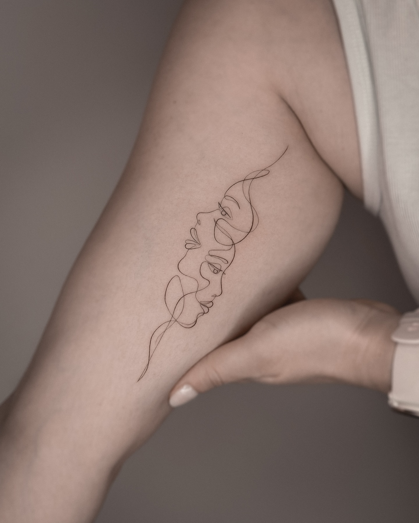 One line vertical faces tattoo along forearm