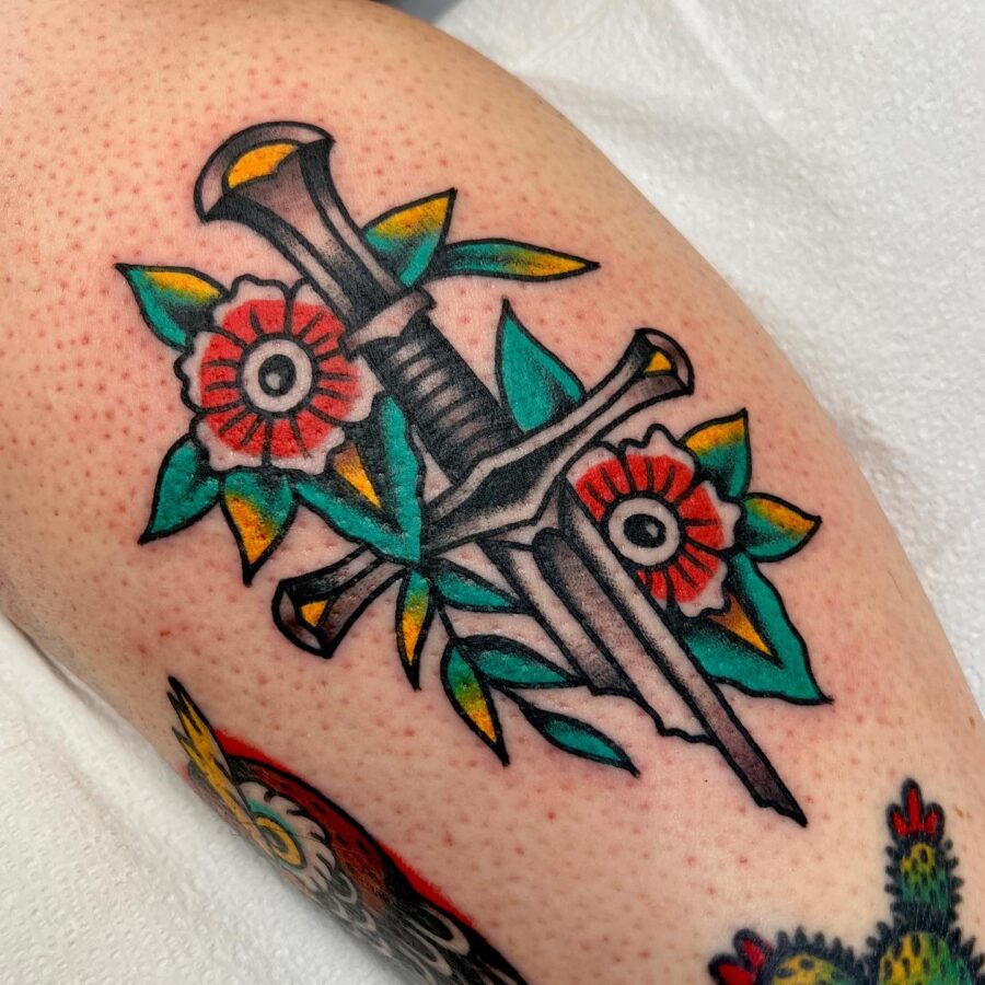 Bold Americana tattoo with dagger and flowers. Tattoo on skin