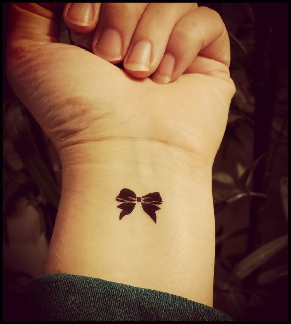 Tiny black bow tattoo on girl’s wrist Tattoo on skin