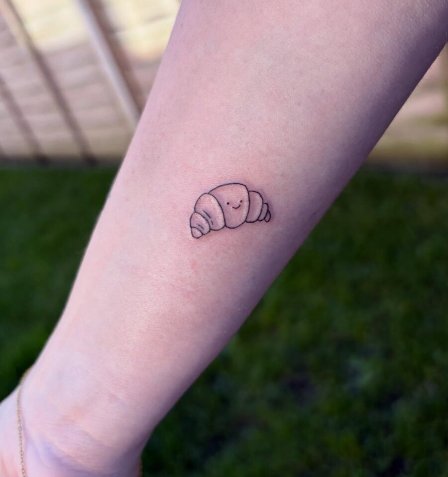Charming croissant tattoo with a whimsical face Tattoo on skin