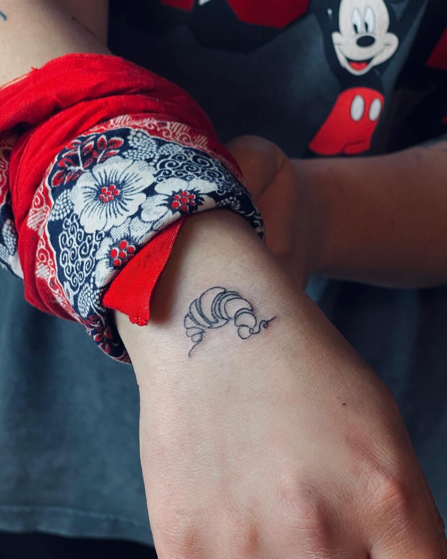 Delicate croissant tattoo on wrist showcases food love Tattoo on skin
