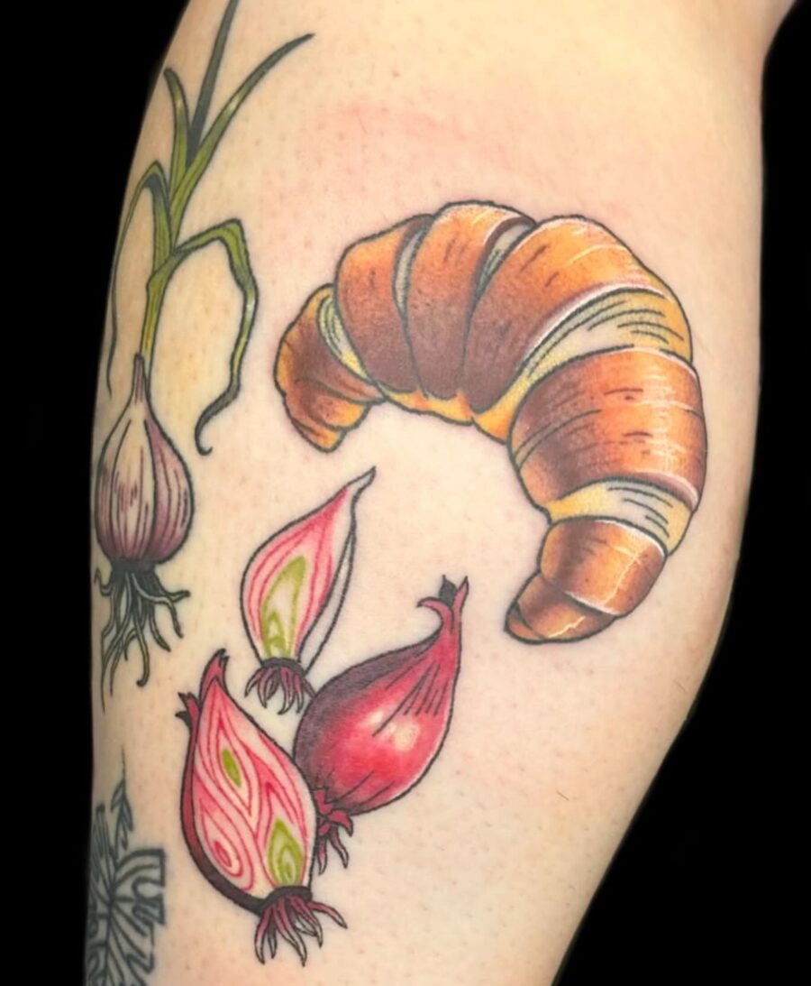 Whimsical croissant tattoo with playful veggies Tattoo on skin