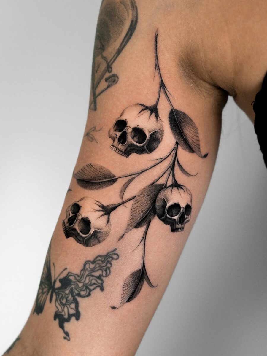 Intricate skulls interwoven with delicate foliage. Tattoo on skin