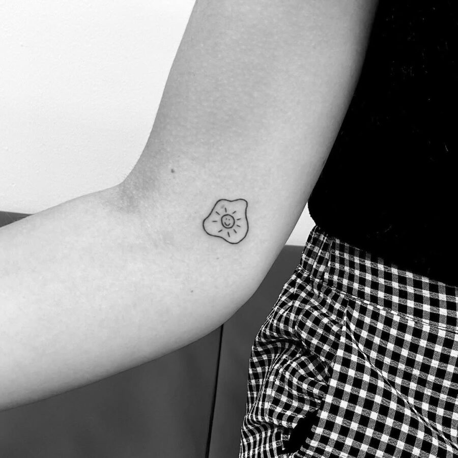 Charming fried egg tattoo with a smiling face Tattoo on skin