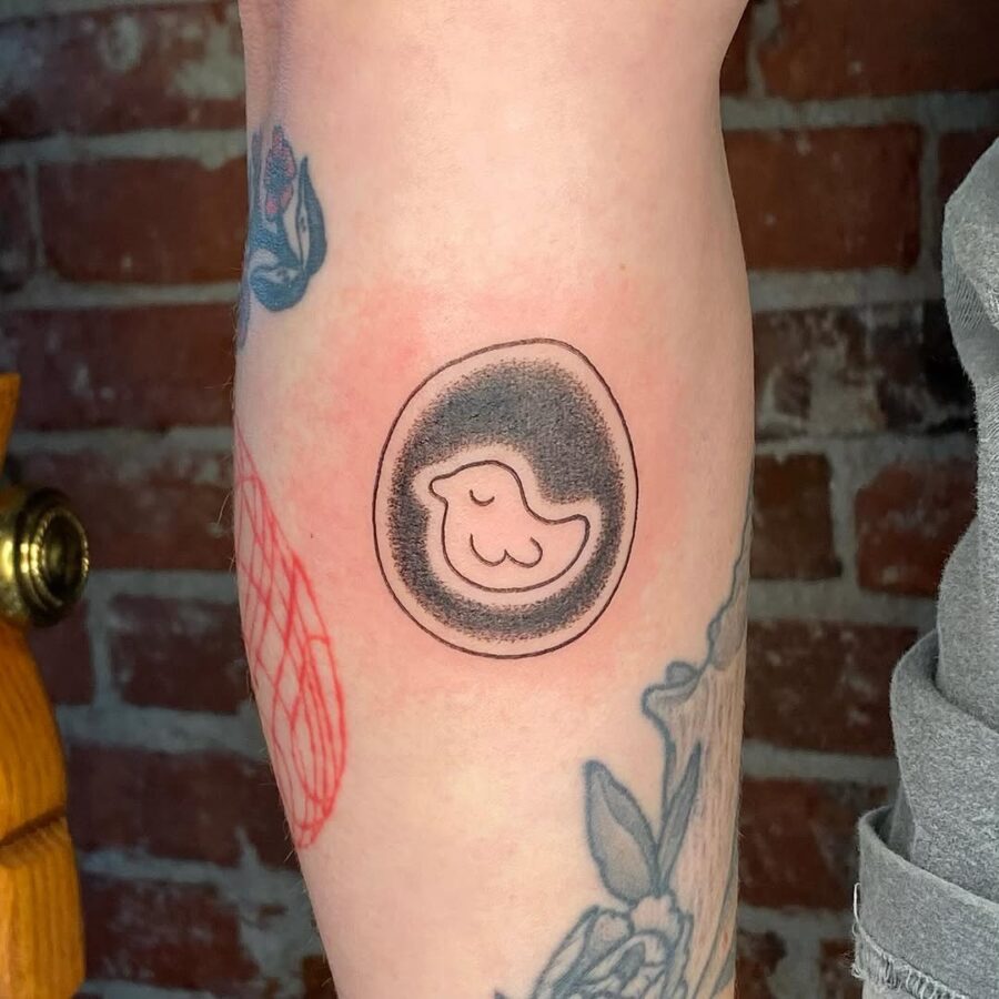 Playful bird in an egg-inspired tattoo Tattoo on skin
