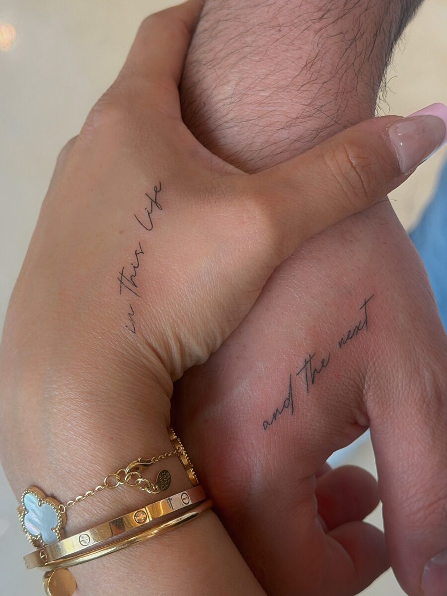 Delicate script tattoos on intertwined hands Tattoo on skin