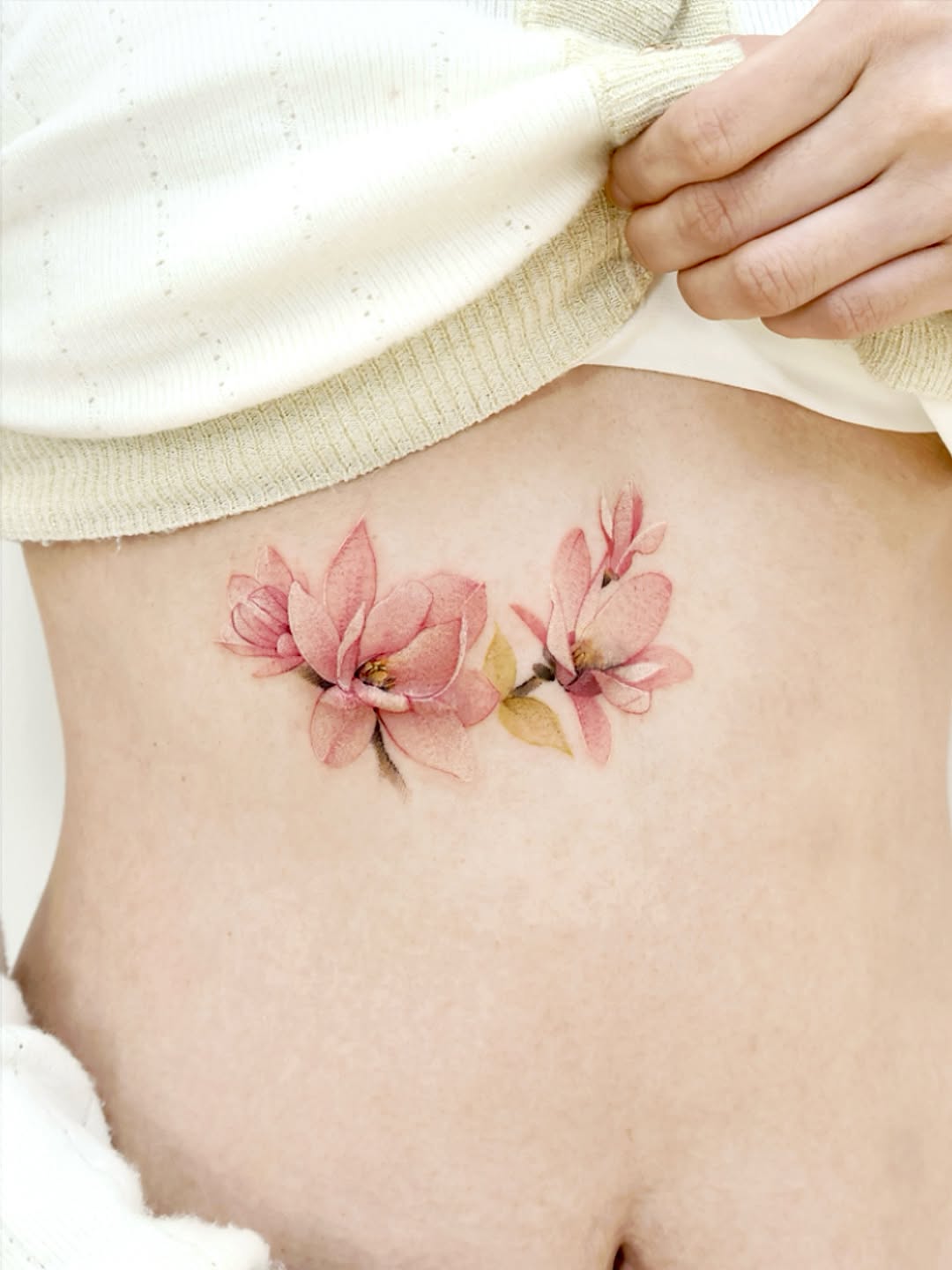 Delicate pink magnolia tattoo on the rib Tattoo on skin