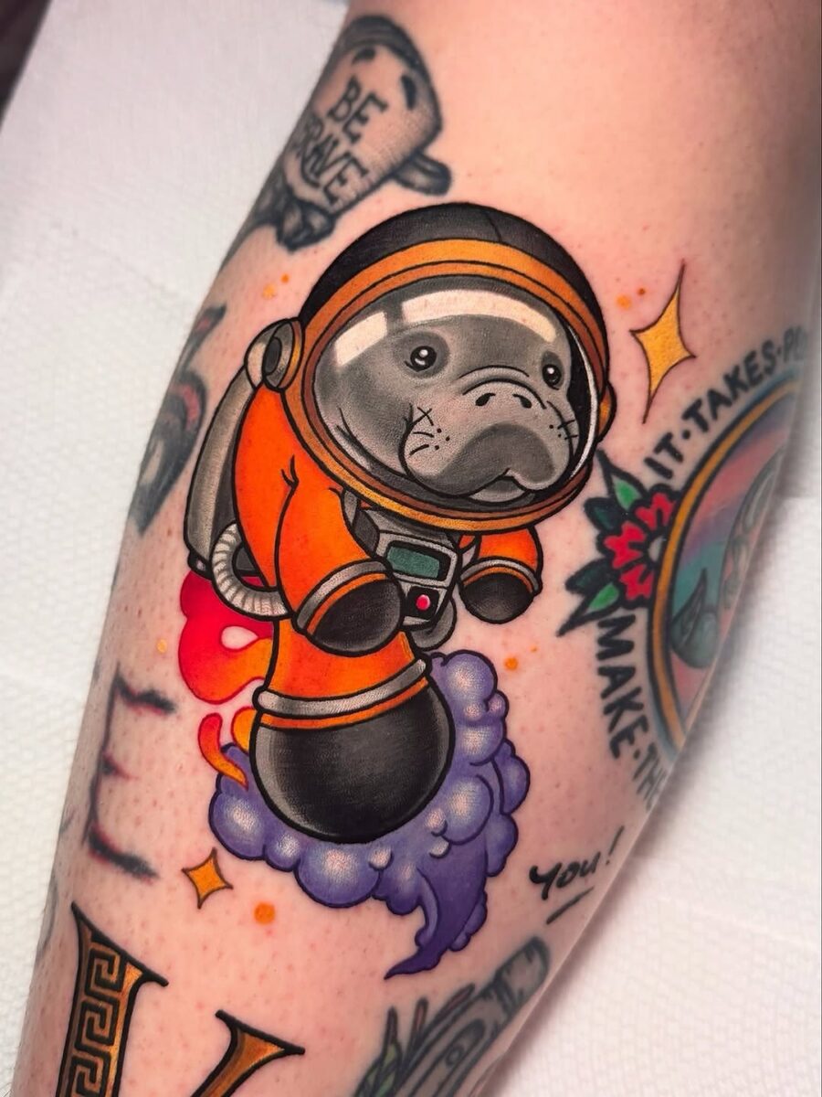 Adorable astronaut manatee tattoo in vibrant colors Tattoo on skin
