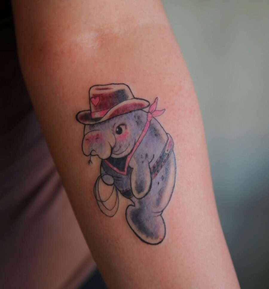 Playful manatee tattoo with cowboy vibes Tattoo on skin