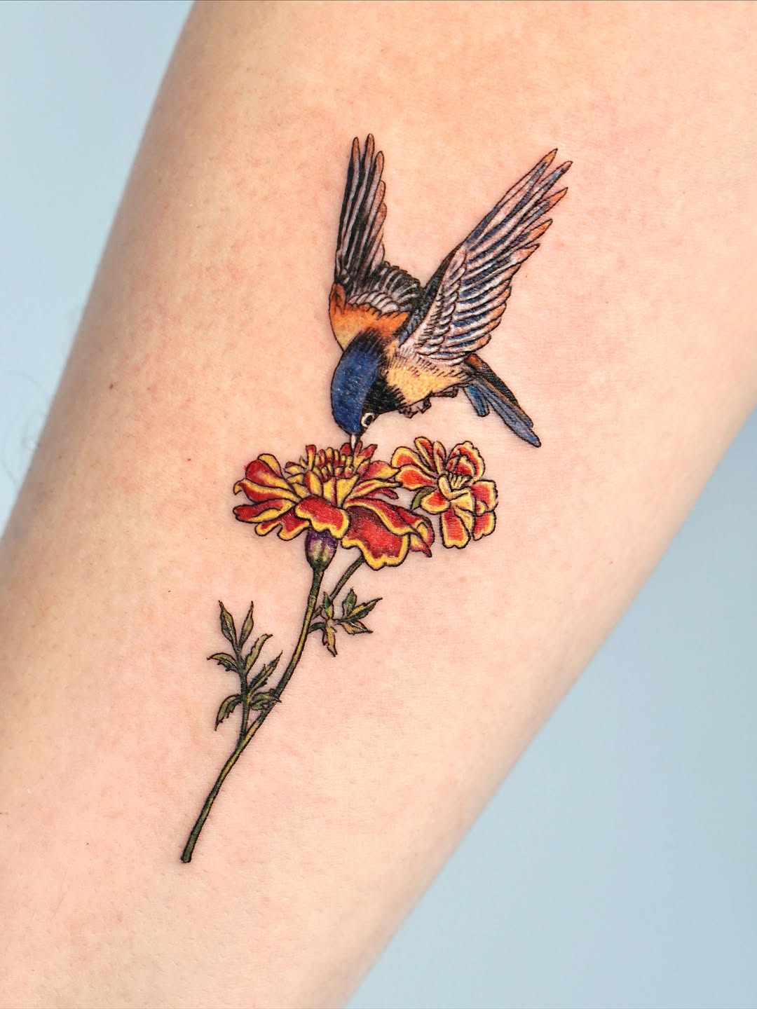 Charming marigold tattoo with vibrant bird detail Tattoo on skin