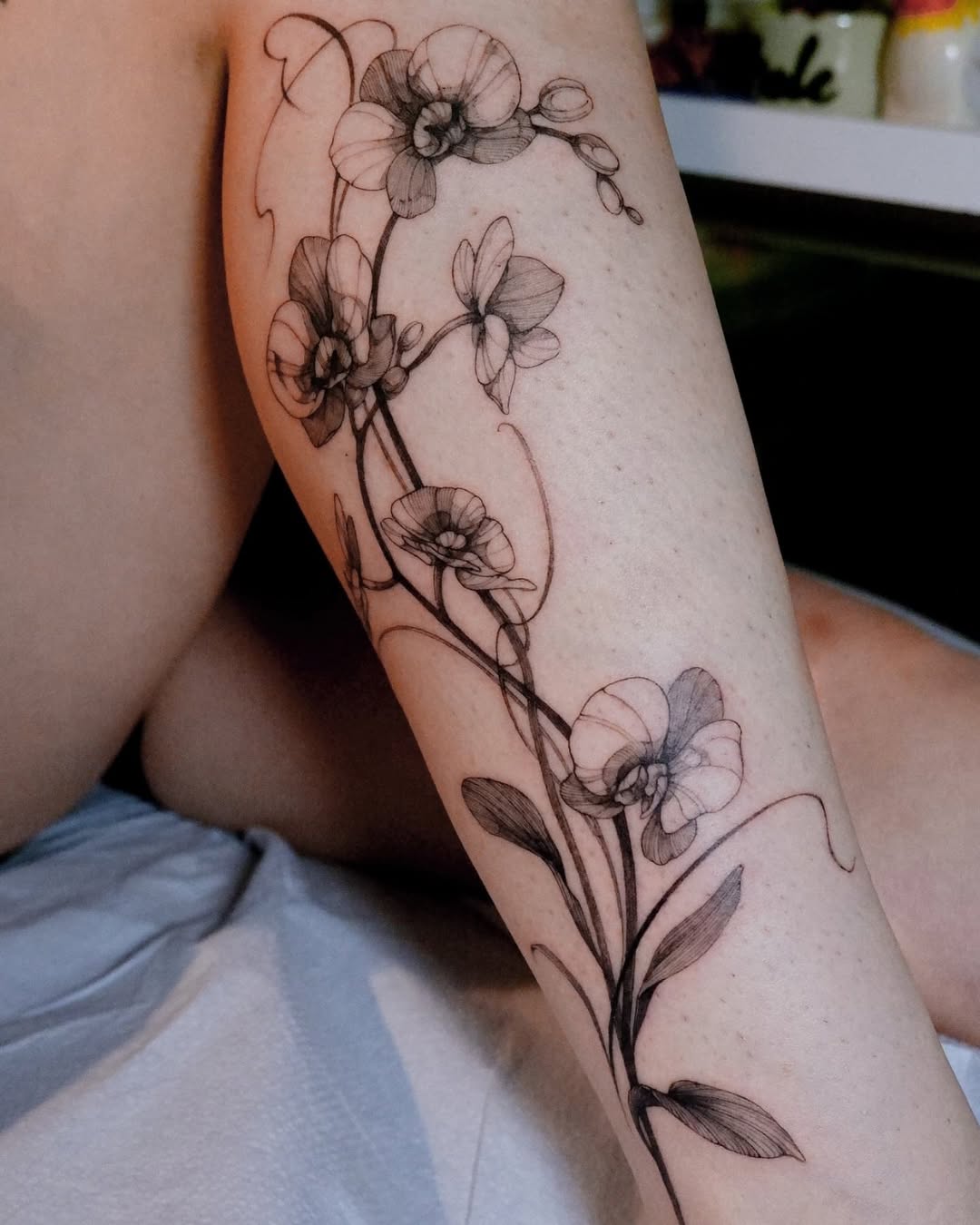 Elegant orchid tattoo wrapping around the leg Tattoo on skin