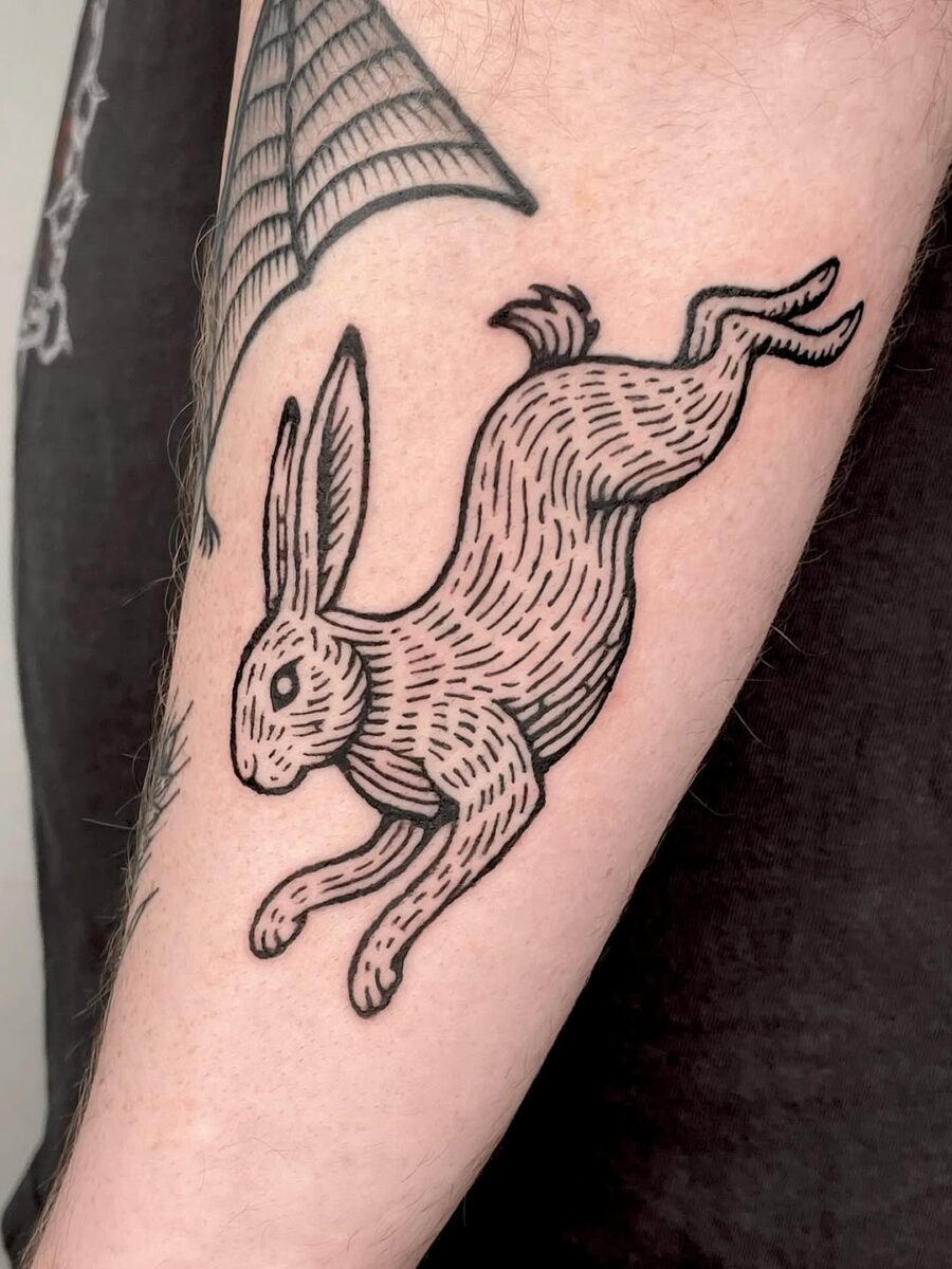 Playful leaping rabbit tattoo in black ink Tattoo on skin