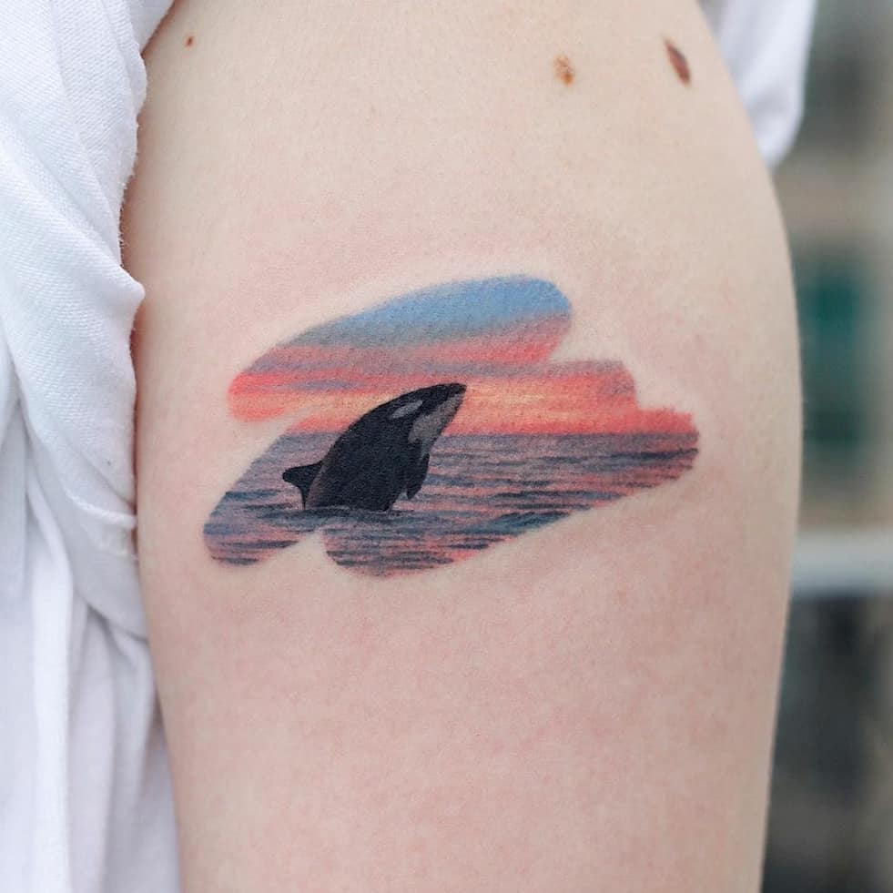 Orca emerging from a vibrant sunset swirl Tattoo on skin